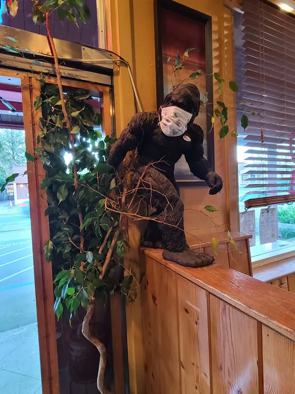 Life-size Bigfoot statue on a knotty-pine railing beside indoor plants at the entrance