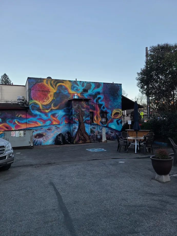 Full-wall psychedelic mural of a fiery sun, a giant redwood and swirling color on the side of the building at dusk